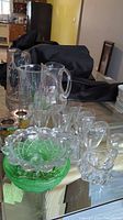 Full view of the lot showing three glass pitchers, assorted glasses, green bowls, candle holders, butter dish, and sugar bowl arranged on a table
