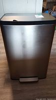 Front view of rectangular stainless steel trash can with foot pedal and soft-close lid showing marks and dents on the surface.