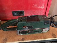 Photo of Bosch PBS 75 belt sander on wooden surface in front of a red toolbox, showing overall condition and size.
