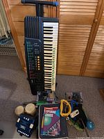 Photo showing the entire lot with Casio keyboard on stand, harmonicas, tambourine, maraca, bongos, two cassette tapes, and music books including 'Exploring Chords'.