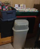 Stack of wrapping paper rolls arranged horizontally in storage bins, with bows in a blue plastic container on top and a tall clear plastic bin in front.