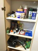Inside cupboard showing shelves filled with workshop supplies including tape, zip ties, sandpaper, and more