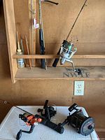 Four fishing reels and fishing jigs on a white Rubbermaid cooler in a garage. One reel mounted on a rod attached to a rack.