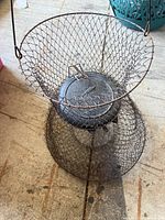 Collapsible metal wire fishing basket showing wire mesh basket, metal lid embossed with bird logo, and metal handle