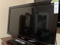 Samsung flat screen TV with remote control sitting on a wooden surface, screen off, with Samsung branding visible on bezel.