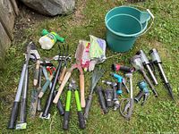 Wide view of all garden tools including pruners, clippers, trowel, rake, sprayers, gloves, bucket and solar lights spread on grass
