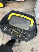 Close-up of the metal detector control panel showing Quick Shooter branding, screen, and buttons for notch, disc, sensitivity, volume, and headphone jack.