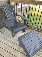Angled front view of one charcoal grey wooden Adirondack chair with slatted seat and back, shown on porch with railing