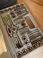 Open tap and die set in gray molded plastic carrying case showing taps, dies, wrenches, and screwdriver neatly arranged.