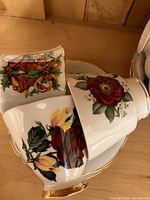 Close-up of floral and holiday patterned tea cups stacked carefully showing various floral and holiday bell motif patterns with gold highlights.