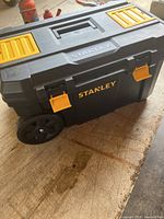 Closed Stanley rolling tool box with yellow latches and black body.