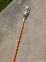 Photo of the full length of the long reach tree trimmer showing the orange pole and the mechanical saw blade cutting head.
