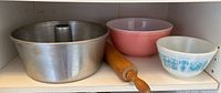 Aluminum angel food cake pan alongside two Pyrex bowls and a wooden rolling pin on a shelf.