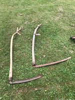 Two antique scythes lying on grass, showing overall shape, handles and blades.