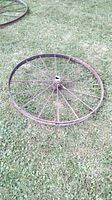 Full view of antique iron wheel on grass showing the rust covering surface and multiple spokes