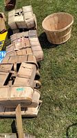 Image of several wood slatted quart baskets stacked together with a single round bushel basket on grass.