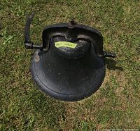 Full view of the black cast metal bell with mounting bracket placed on grass.