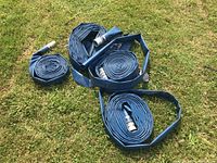 Four rolled blue water pump hoses laid out on grass with metal fittings at hose ends.