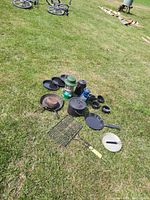 Wide angled view of all cookware items on grass: includes cast iron pans, mesh screens, lanterns, plates, and cups.