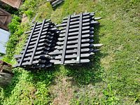 Two stacks of black painted wooden picket fence sections on grass, showing pointed vertical slats and horizontal rails.