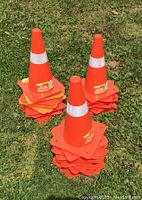 Three stacks of orange safety cones placed on grass, each cone 12 inches tall with a white reflective band and square base.