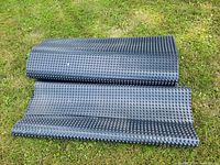Roll of black sealing membrane with textured raised circular bumps laid on grass.