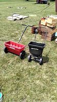 Both seed spreaders on grass, one red and one black, showing overall shape and size
