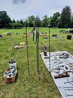 Four wrought iron shepherd's hooks standing in grass near a table with various tools and items, showing the full height and shape of the hooks.