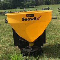 Front view of the yellow SnowEx lawn spreader showing brand logos and hopper shape.
