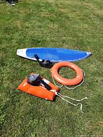 Overview photo of surfboard, snorkel mask, life saver jacket, and life saver ring laid on grass.