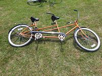 Side view of the entire orange tandem bicycle lying on grass