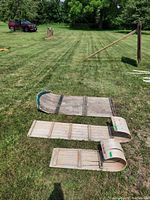 Three wooden toboggans laid out on grass: one large 4-seater and two smaller 2-seaters with visible weathering and metal reinforcements on curved fronts.