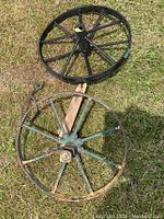 Photo of two vintage wagon wheels on grass; one black painted with 6 spokes, and one rustic blue-green painted with 8 spokes and wooden brace.