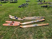Four pairs of vintage water skis laid out on grass with visible bindings and wear.