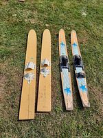 Four water skis laid out on grass, two wooden with white bindings and two Starfire skis with blue star graphics and black bindings