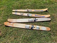Top view of four wooden water skis laid on grass, two pairs with bindings visible. Brands Mermaid and Starfire painted on skis.