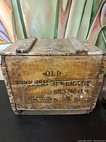 Front view of the wooden crate showing the branded text and lid closed, displaying wear and aged wood.
