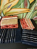 Four decorative towels displayed, showing two patterned red/tan/white and two navy blue striped towels.