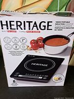 Closed Heritage induction cooktop box showing product labeling and imagery of the cooktop and saucepan with tomato-based soup.