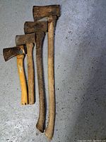 Four axes of varying sizes laid on a floor, showing the front view including handles and blades with rust and wear.