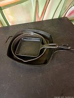 Lot of three cast iron pans stacked on top of each other, showing different sizes and shapes.