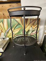 Front view of a black metal vintage plant stand with a round base shelf and curved legs.