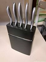 Overall view of black knife block holding five knives with stainless steel curved handles.