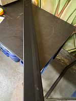 Full length view of the long rectangular black soundbar with a mesh grille on top and front, placed on a dark surface.