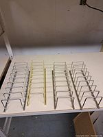 Four heavy metal storage racks shown on white surface; three silver finish, one gold finish, multiple vertical wire dividers in each rack.