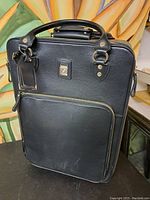 Front view showing black leather travel bag with front zippered pocket and handles.