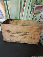 Shows the full view of the rectangular vintage wooden crate with black printed text identifying manufacturer and locations.