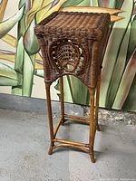 Wicker jardiniere stand showing front side with decorative wicker circular pattern and wooden legs
