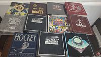 Photo showing front covers of 11 sports card binders laid flat on a white surface, depicting various themes in baseball, hockey, and football collection albums