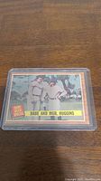 Photo of 1962 Topps Babe Ruth Special baseball card featuring Babe Ruth and manager Huggins, displayed in protective plastic sleeve on wood surface.